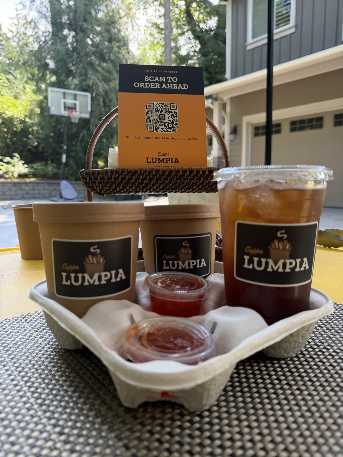 Kraft cups labeled with the Cuppa Lumpia logo, an order-ahead card, and iced tea in a basket at the driveway stand